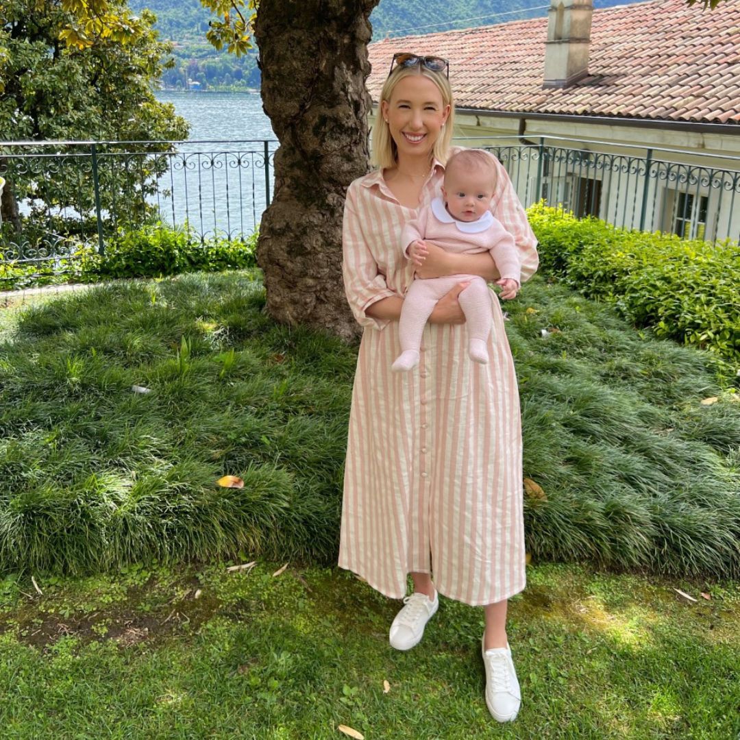 A mother with a beautiful baby girl smiles in her room and wears The Mary Long Shirt Dress with Pink Stripes