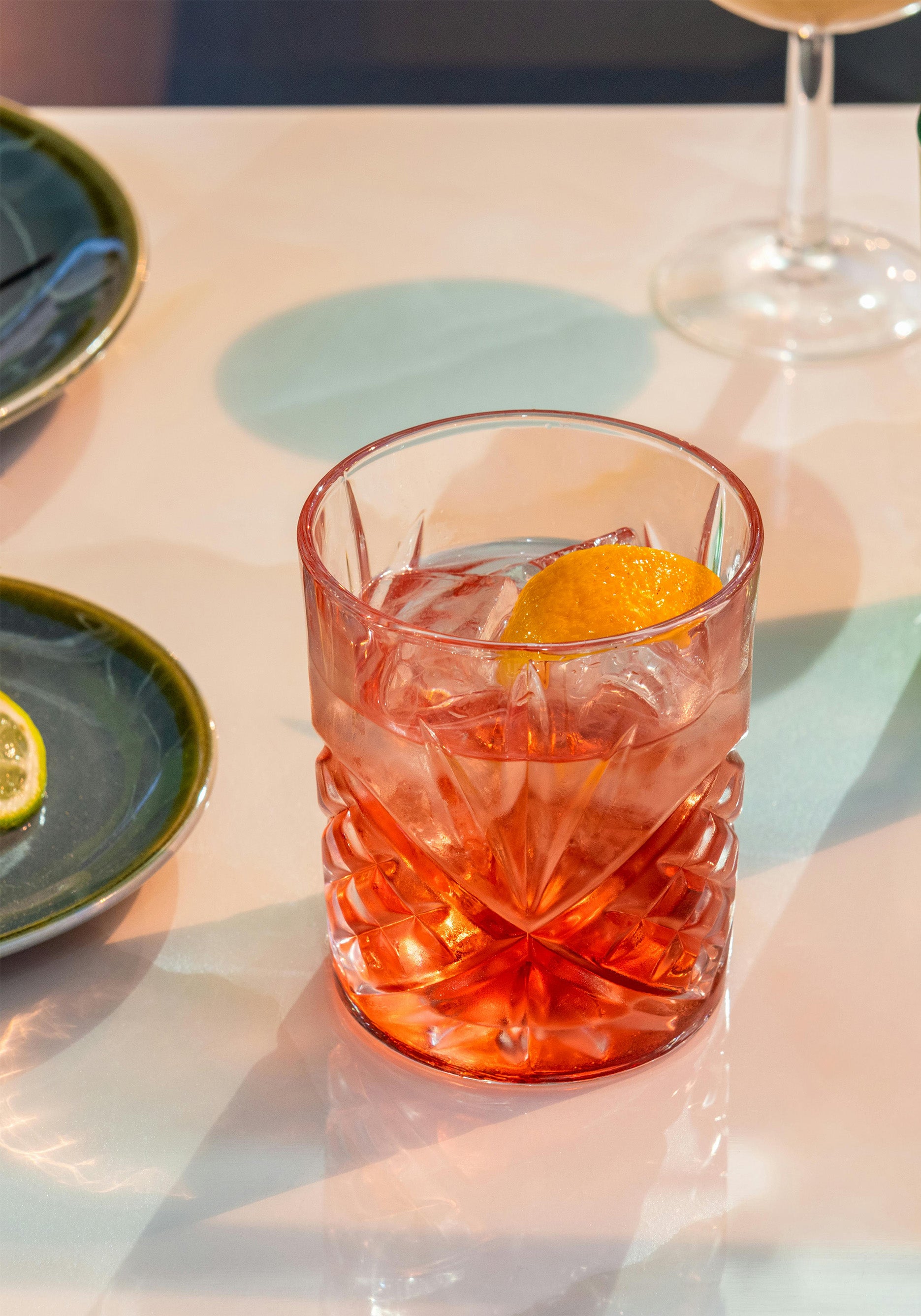 Glass tumbler on top of a table with negroni drink and orange wedge in it 