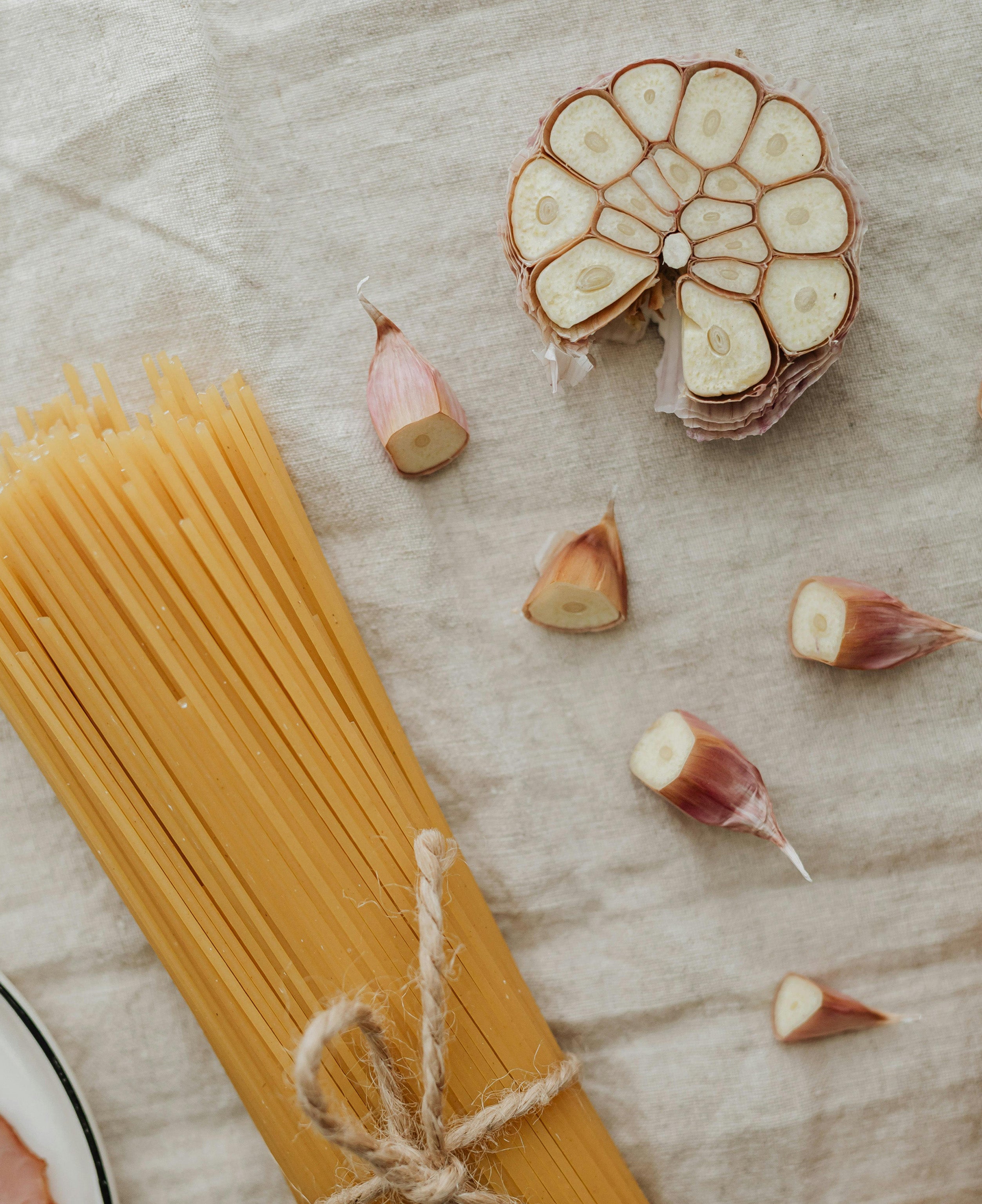 Bunch of noodles tied by string over a tablecloth with garlic wedges next to it
