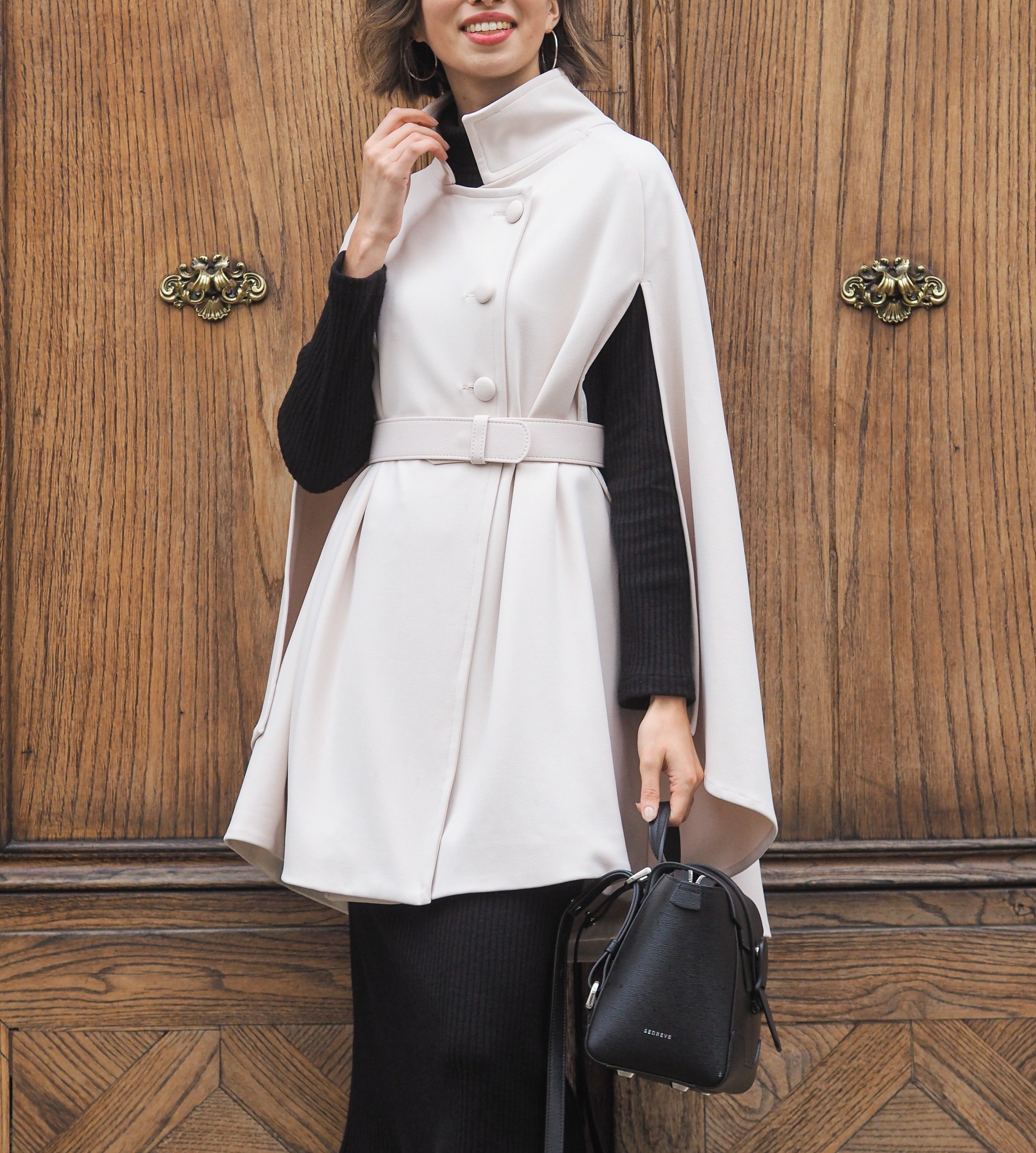 Vanessa wears Marta Scarampi's cream-coloured cape model The Rachel Mondrian with extraordinary elegance. She matches the cape with a dark suit and a black handbag. 